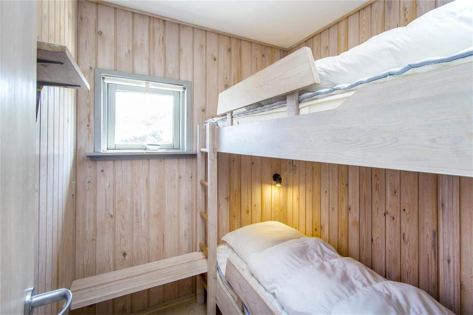 Zimmer mit Doppelstockbett, Holzwand und kleinem Fenster.