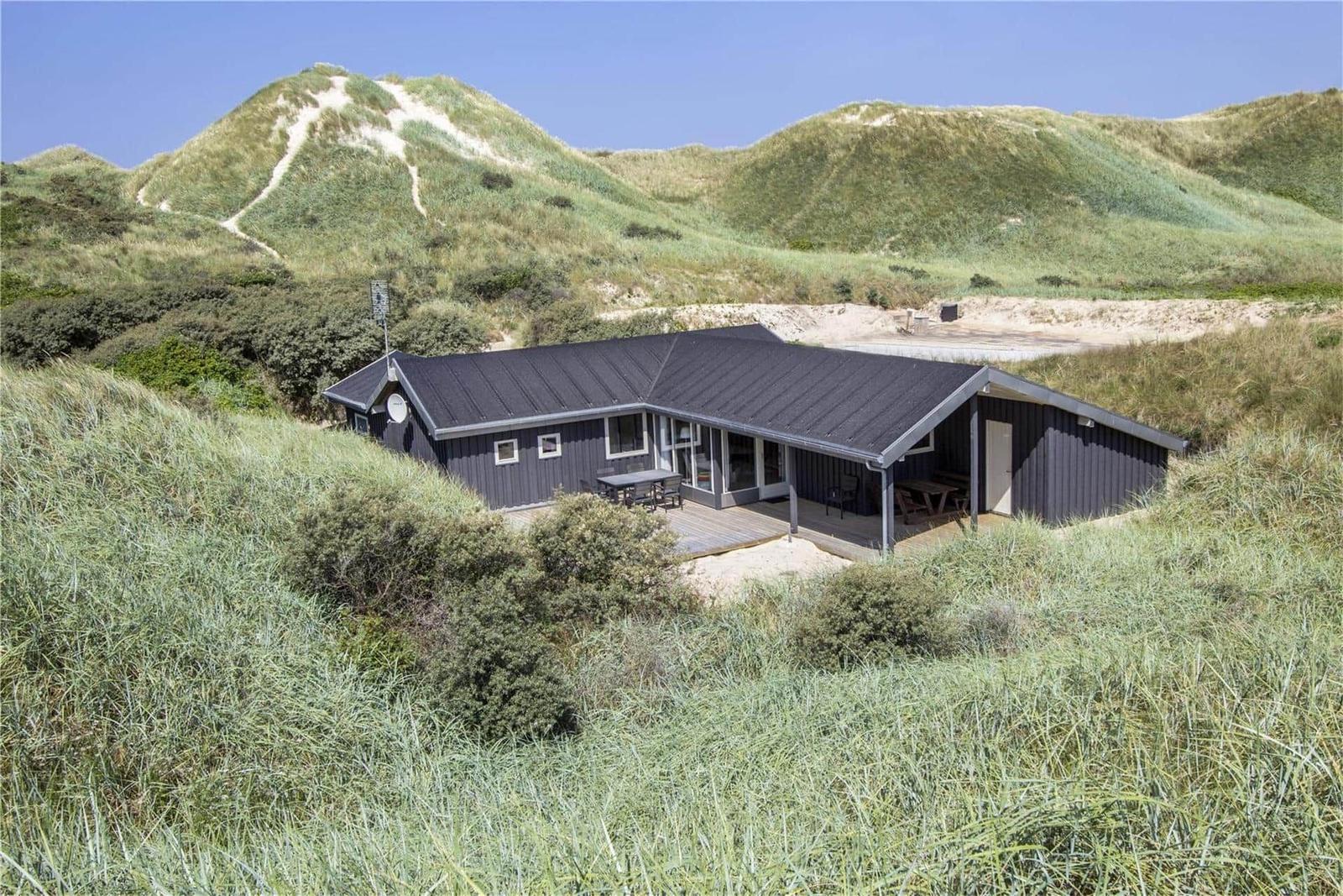 Moderne Hütte mit Terrasse zwischen grünen Dünen und Sandhügeln.