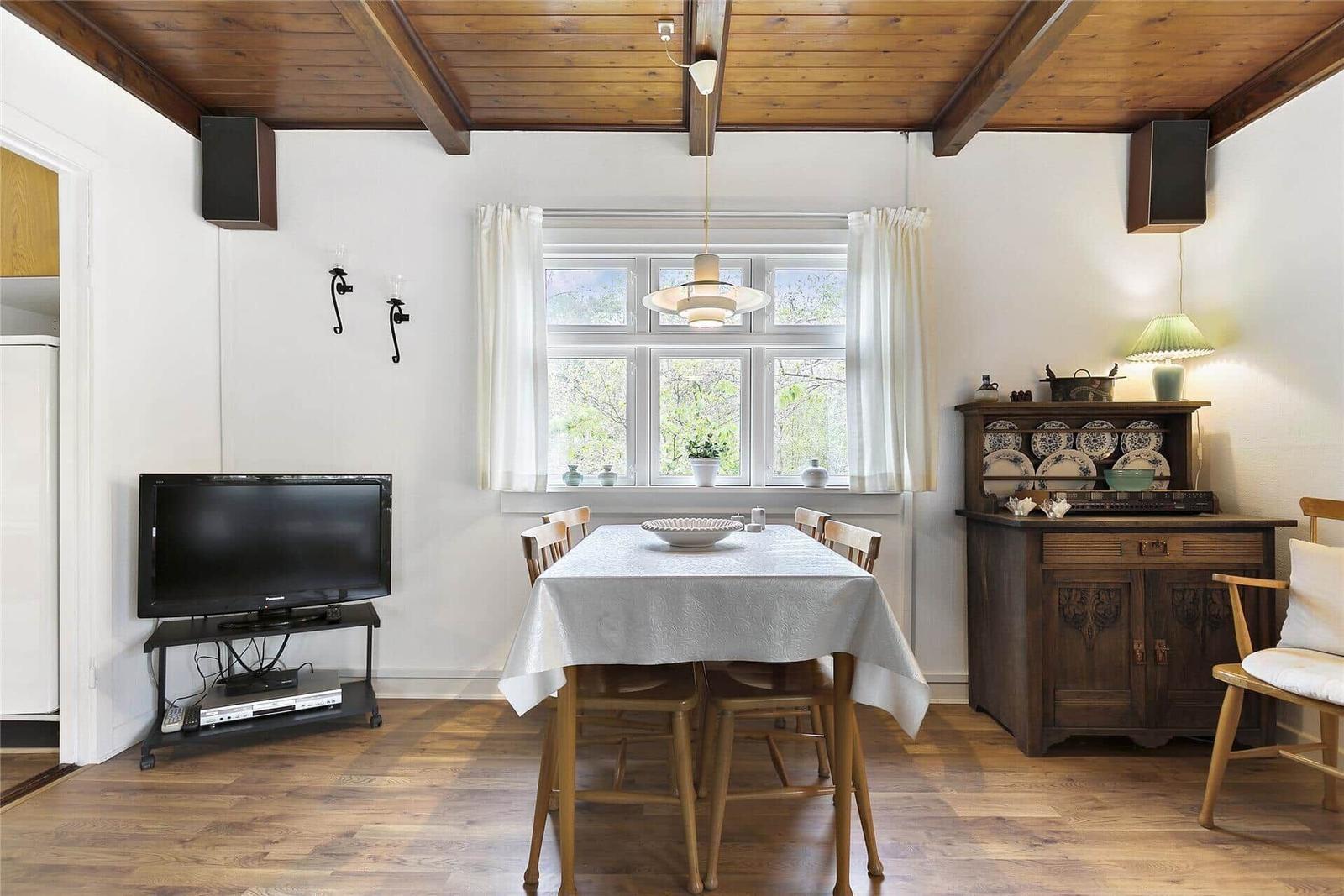 Esszimmer mit Tisch, Stühlen und Fenster. Holzdecke und -boden. Fernseher und Sideboard.