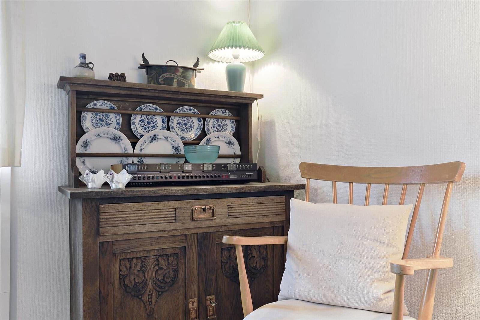 Holzschrank mit Tellern, Lampe und Stuhl mit Kissen.