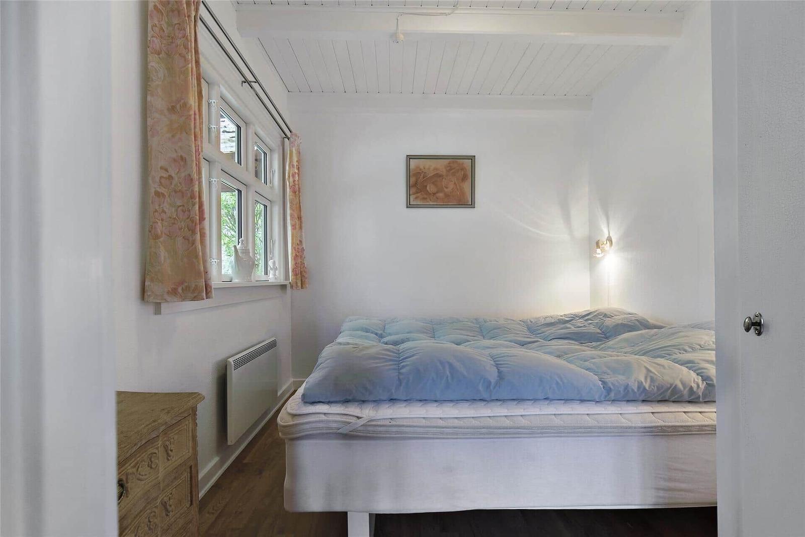 Schlafzimmer mit Bett, Fenster, Gardinen und Wandbild.