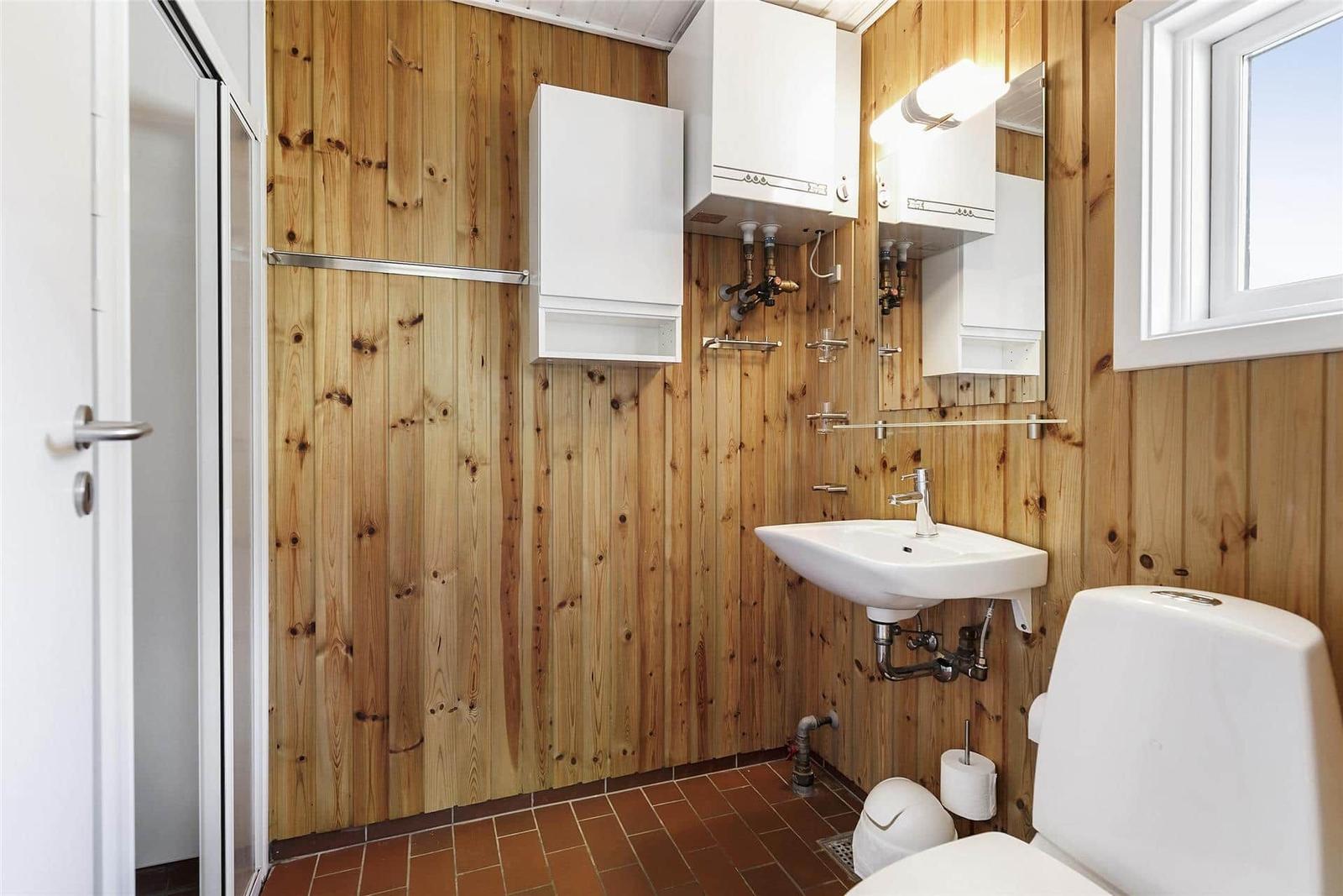Badezimmer mit Holzwand, Waschbecken, Toilette und Dusche.