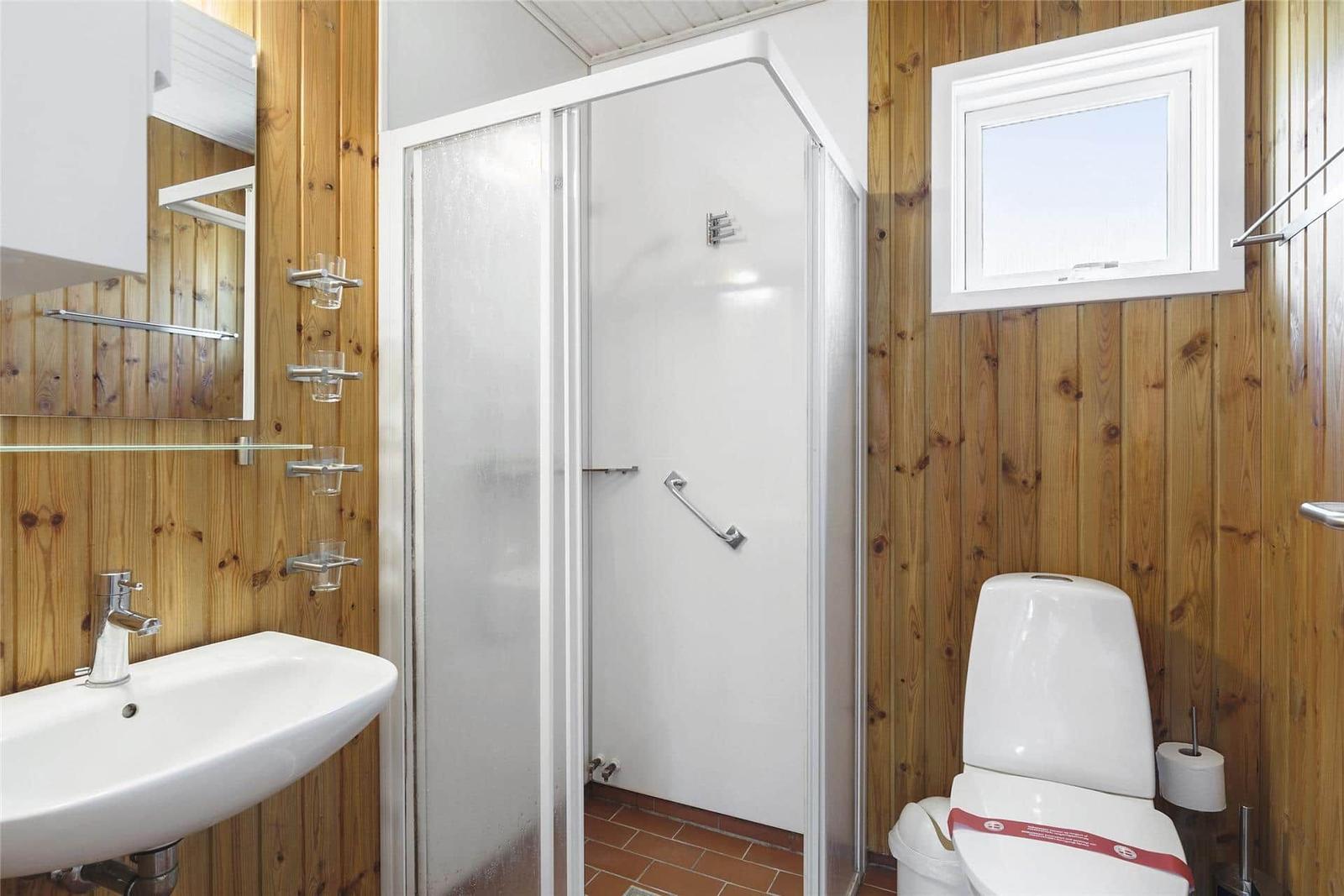 Bad mit Dusche, Waschbecken und Toilette. Holzwandverkleidung und Fenster.