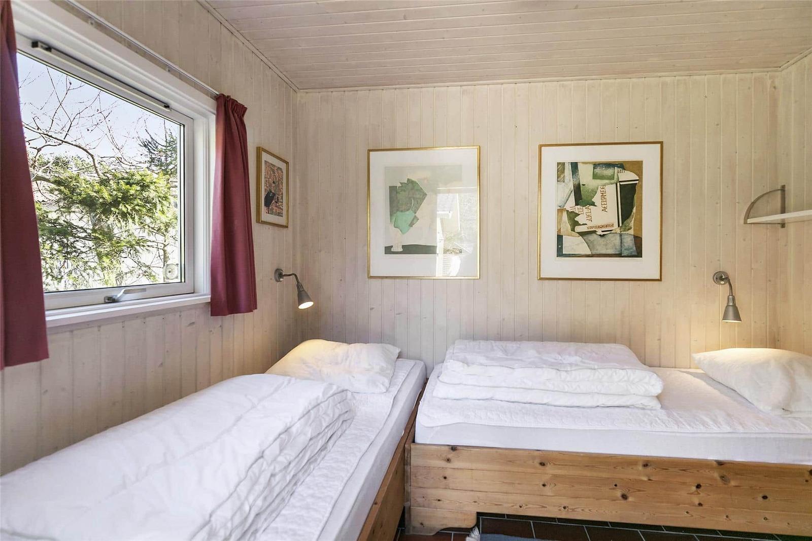 Zwei Betten mit weißen Bettwäsche, Holzwände und Fenster mit Blick auf Bäume.