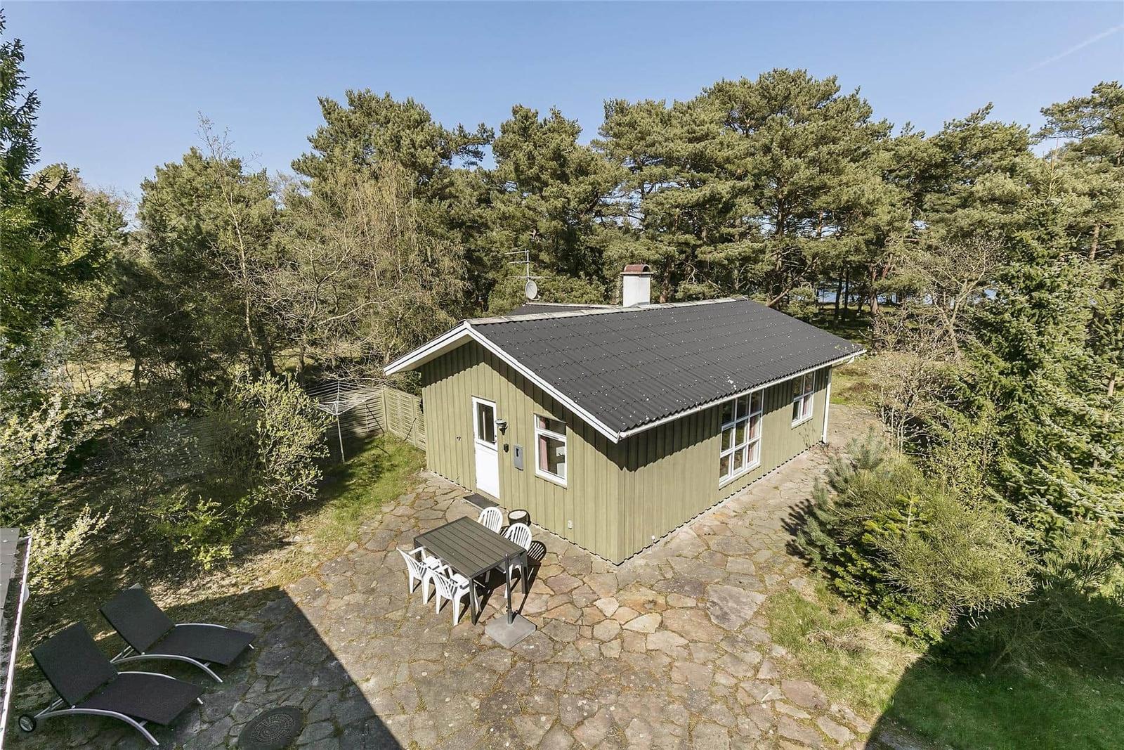Ein grünes Haus mit Steinplattenhof, Gartenmöbeln und umgeben von Bäumen.