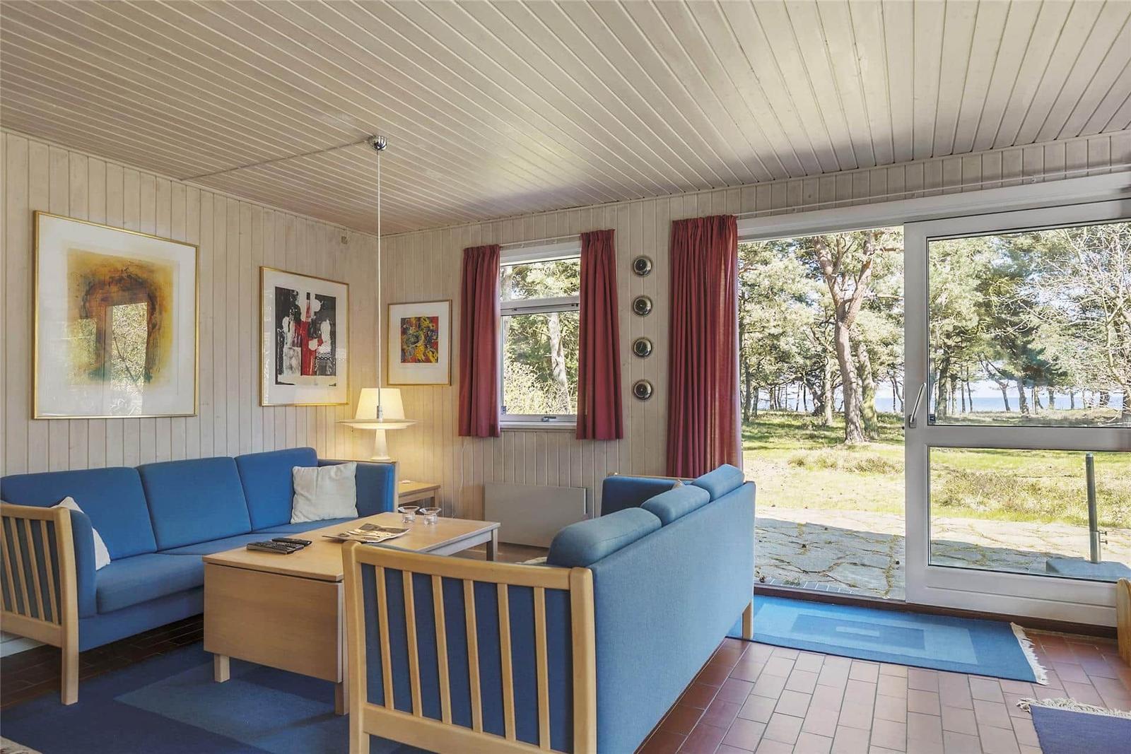 Wohnzimmer mit blauen Sofas, Holztisch und Blick auf Grünland und Bäume.