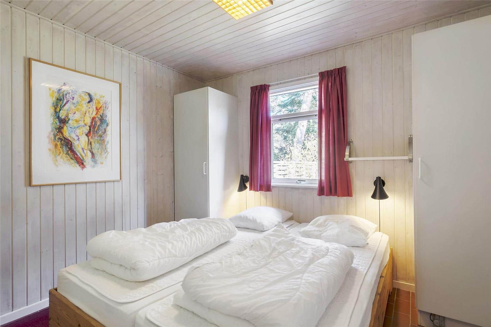 Schlafzimmer mit Doppelbett, Fenster mit roten Vorhängen und Wandbild.