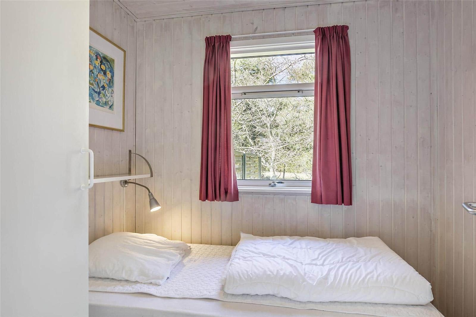 Schlafzimmer mit Bett, Fenster und roten Vorhängen an Holzwand.