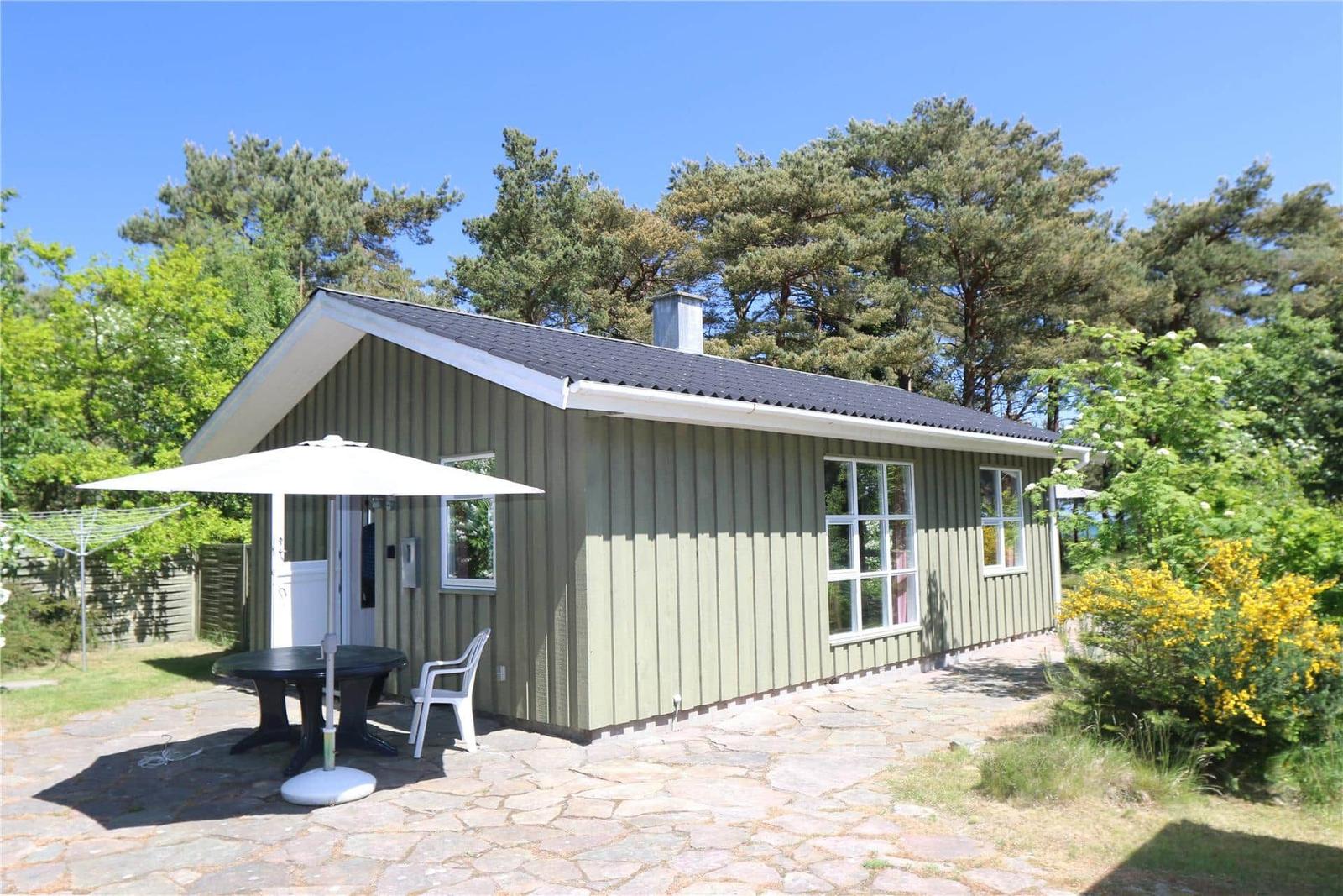 Ein kleines Haus mit Terrasse, Sonnenschirm und Tisch. Umgeben von Bäumen und Sträuchern.
