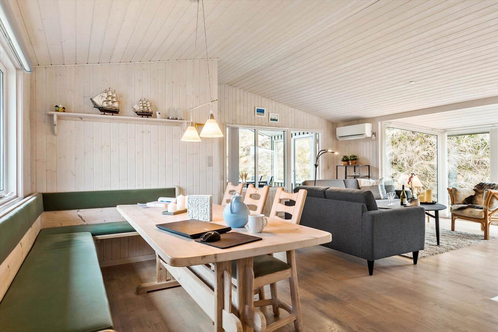 Dining area with wooden table and green bench, next to living area with sofa and large windows.