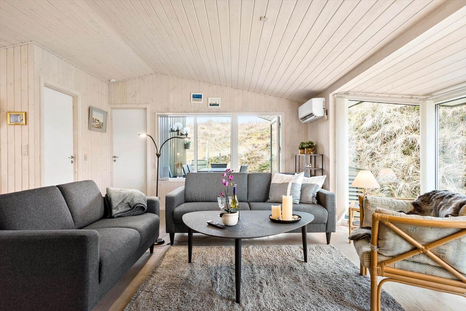 Living room with two sofas, round table, and large windows. Wooden walls and ceiling.