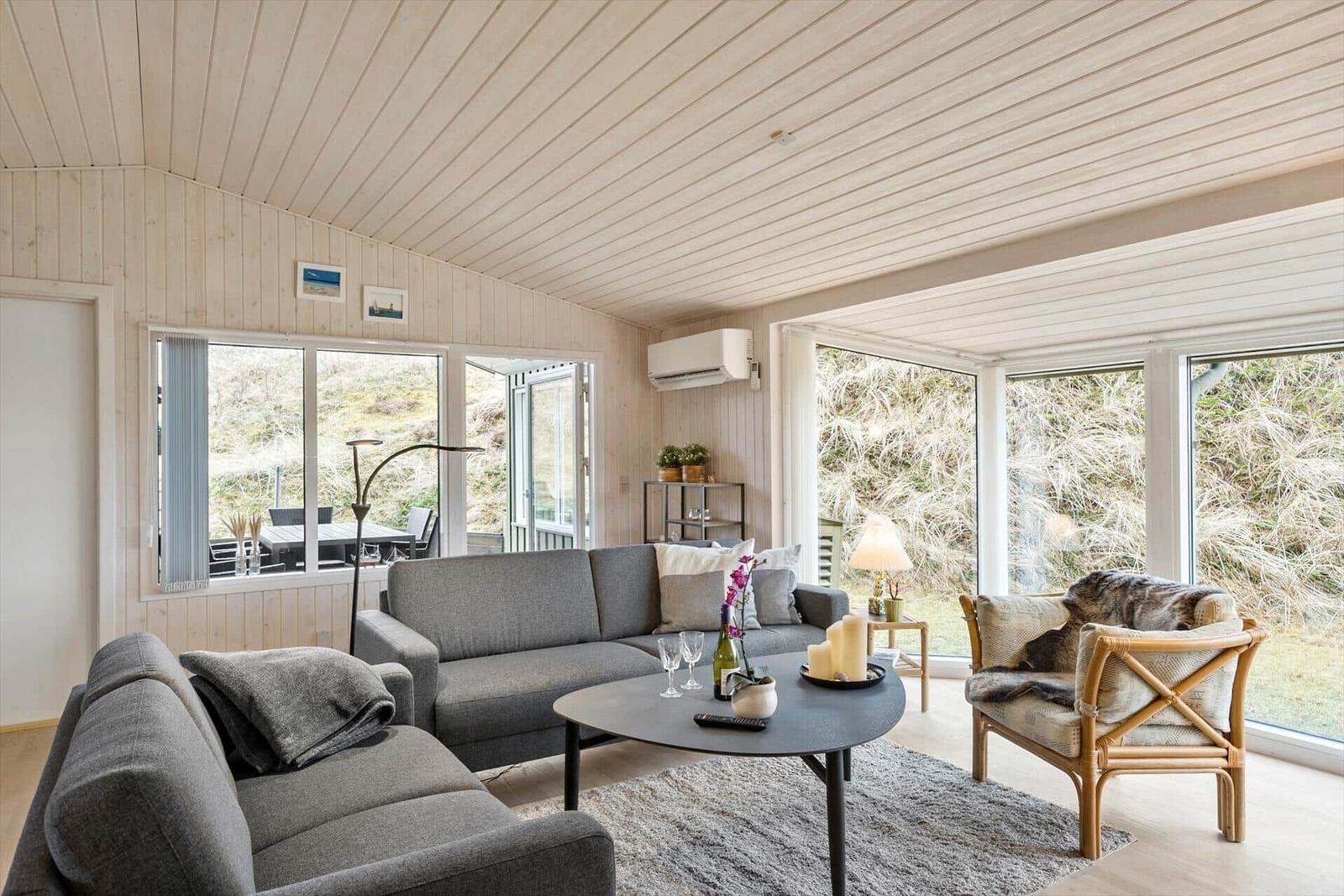 Living room with sofa, armchair, and table. Large windows offer view of outdoor area.