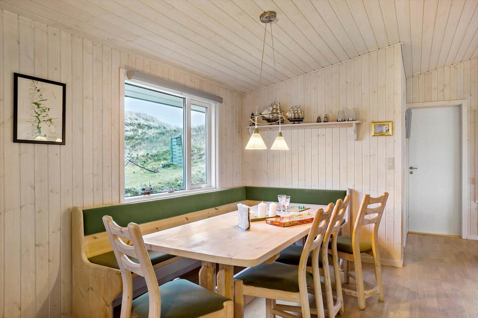 Dining room with wooden table, bench, and chairs. Window shows green landscape.