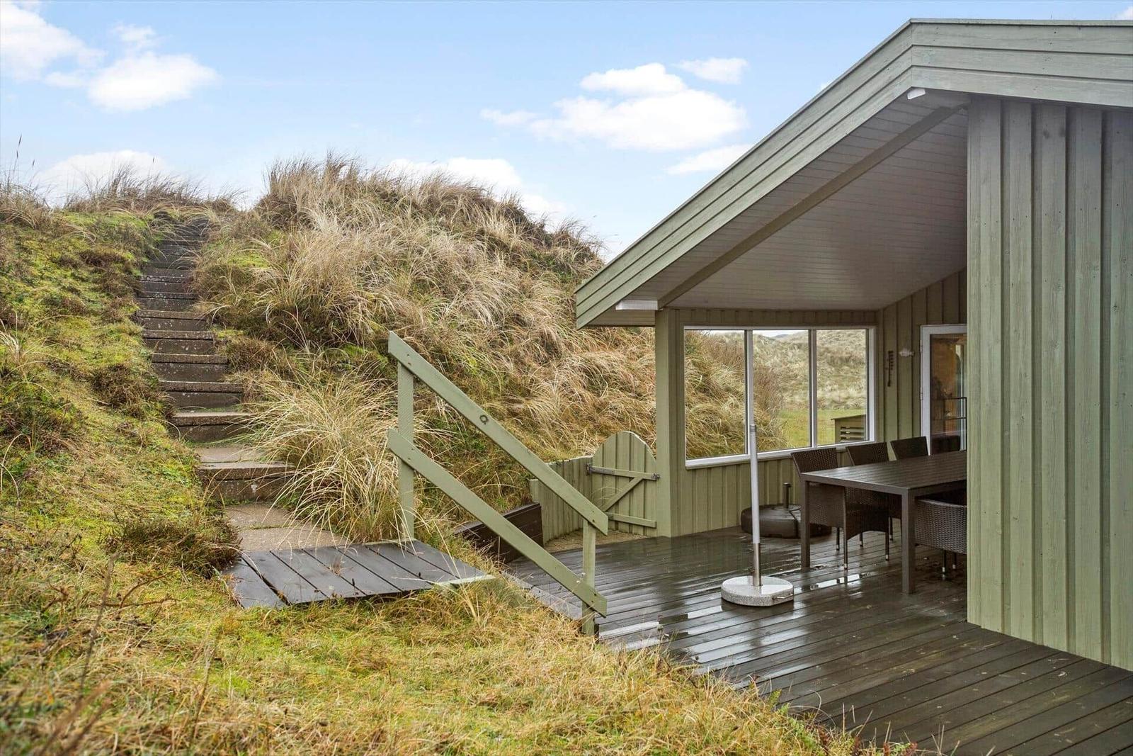 Wooden terrace with table and chairs next to a house with view of dunes.
