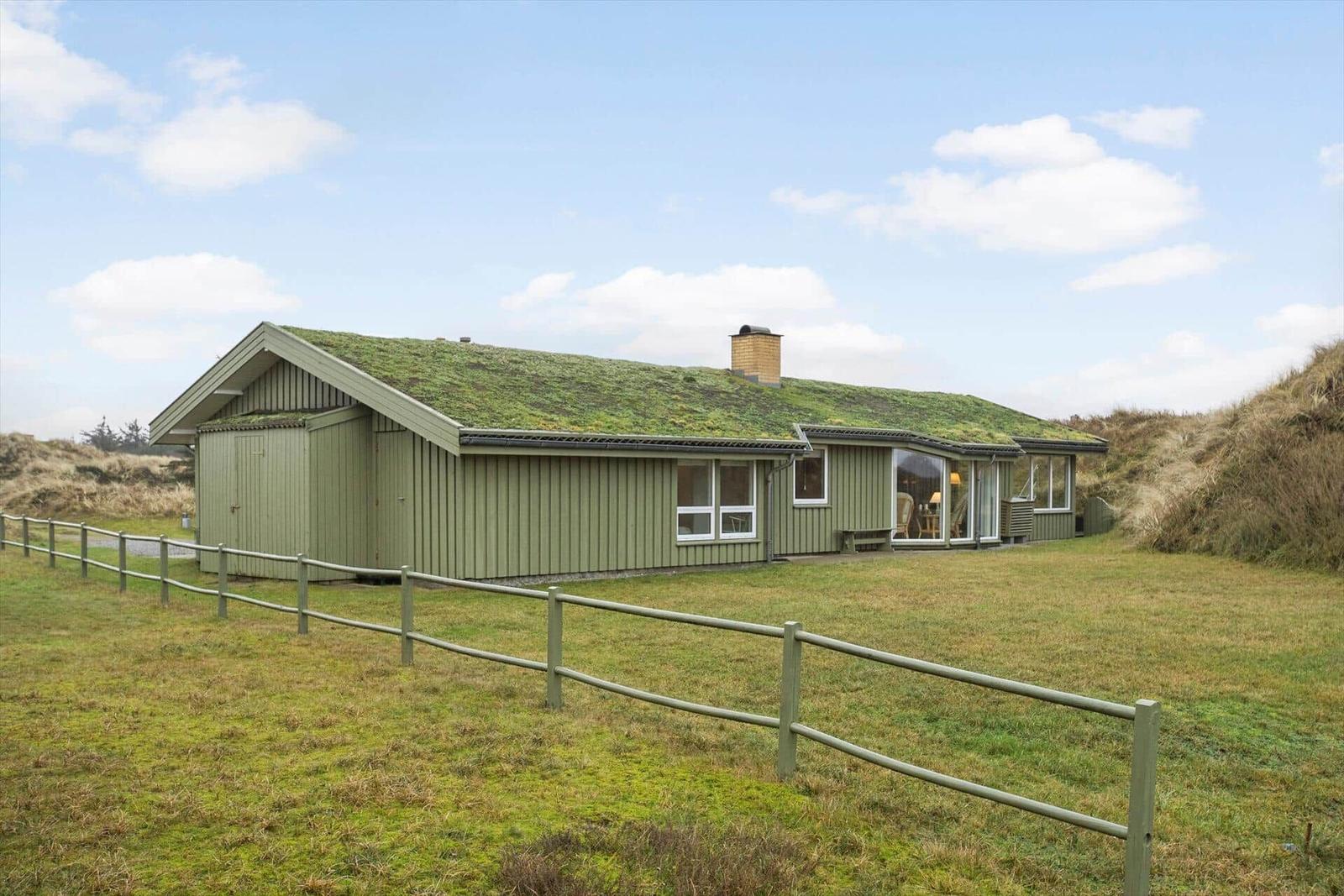 A house with a grass roof and large windows in a rural setting.