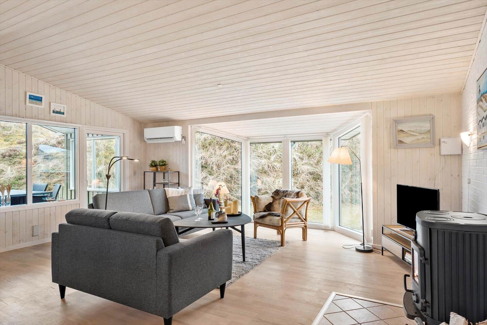 Living room with sofa, armchair, and wood stove. Large windows with view of the landscape.