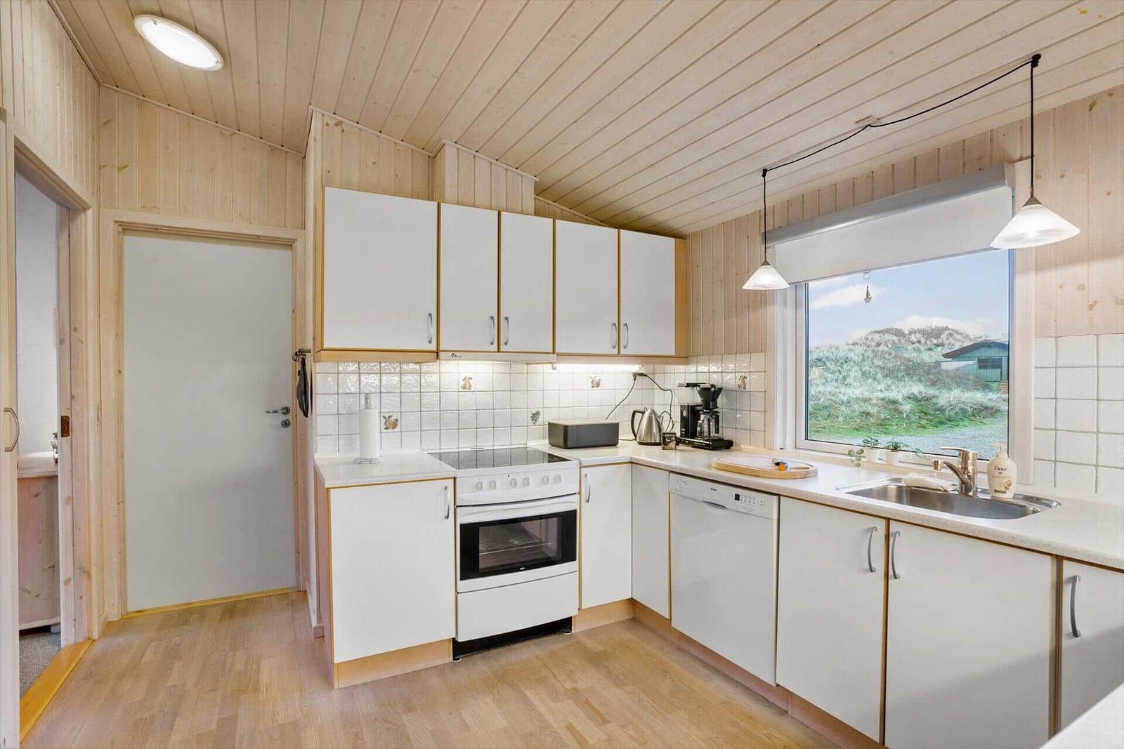 Kitchen with white cabinets, stove, and dishwasher. Window with view of greenery.