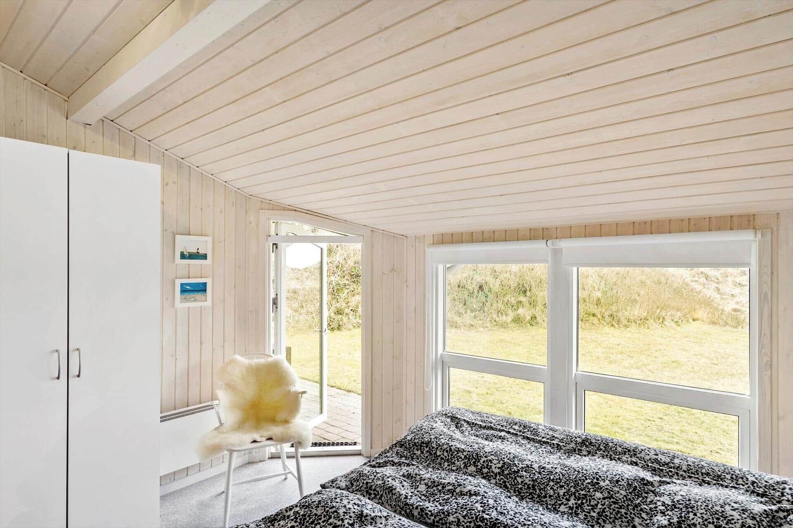 Bedroom with bed, white walls, and windows to the garden.