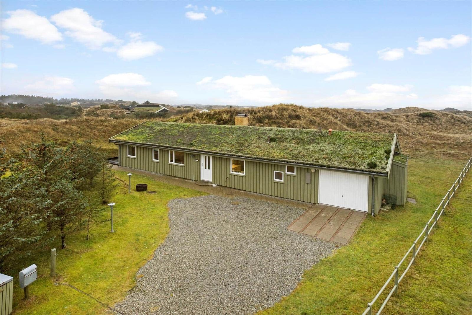 Single-story house with green roof and garage in a grassy area.