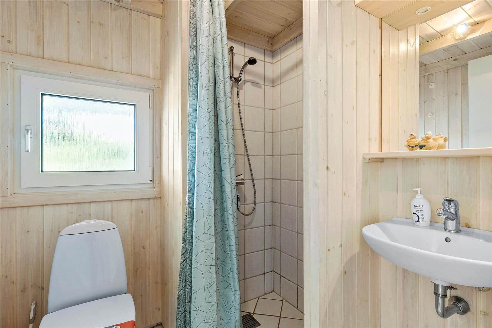 Bathroom with shower, sink, and toilet. Wooden walls and window.