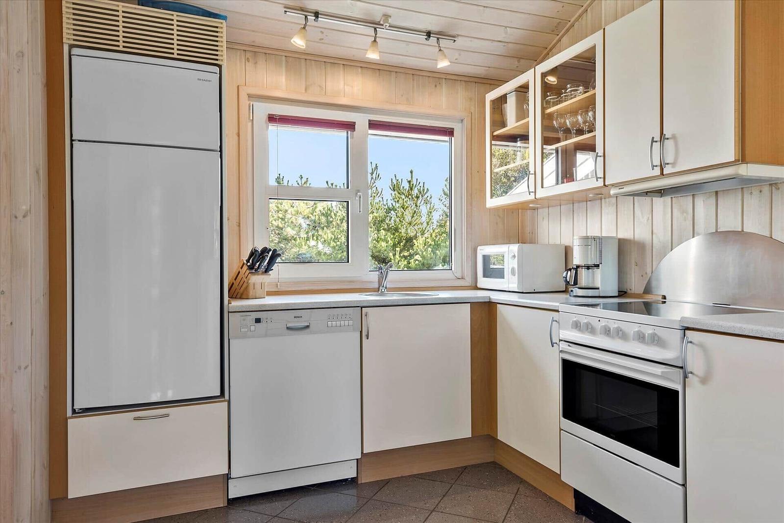 Kitchen with fridge, dishwasher, and stove. Window with view of trees.
