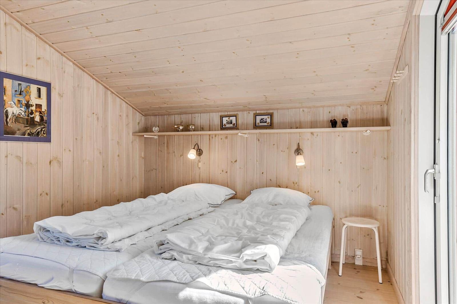Room with wooden walls, double bed, wall lamps, and picture on the wall.