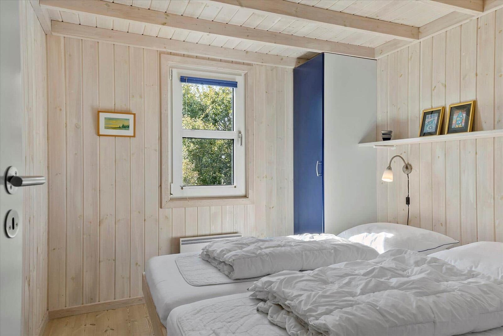 Room with two beds, wooden walls, and window with view of trees.