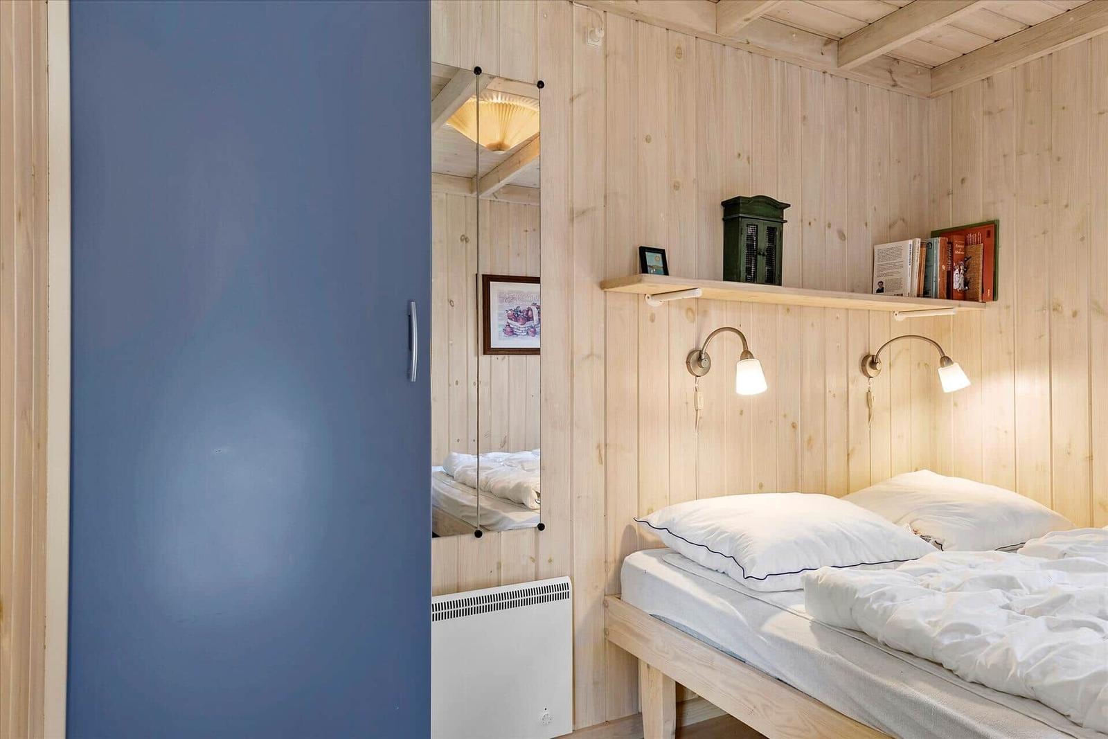 Bedroom with wooden walls, bed, nightstand, and mirror.