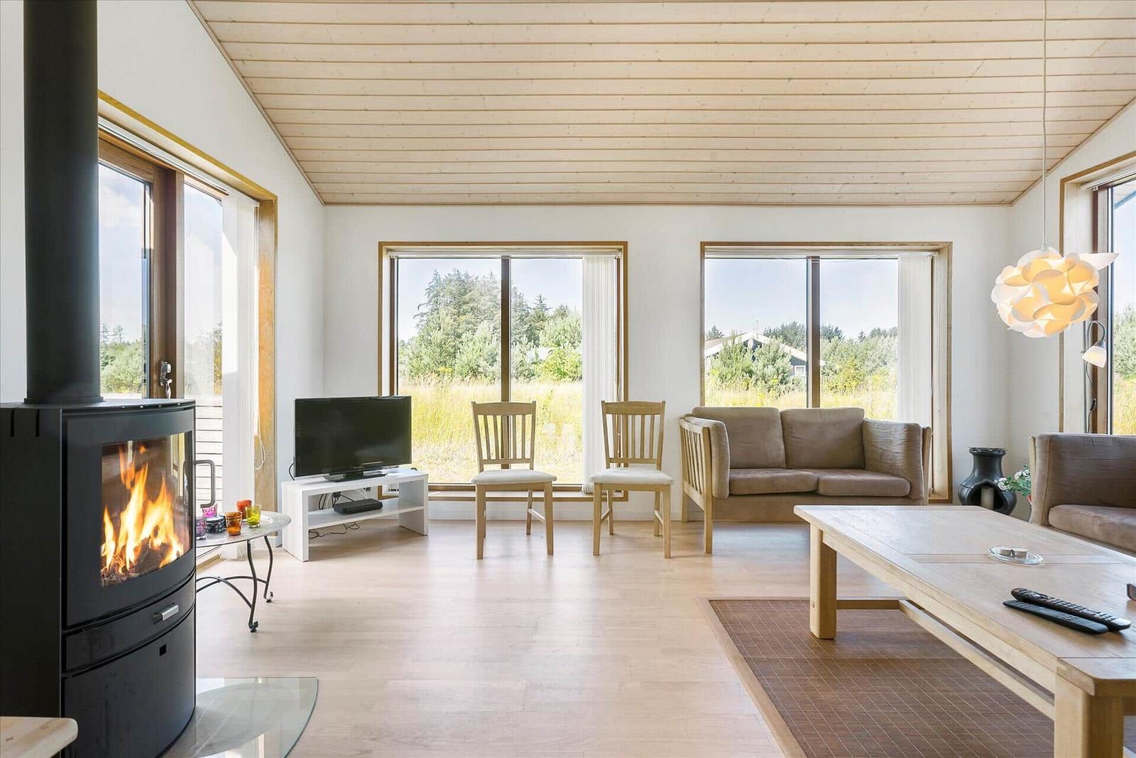 Wohnzimmer mit Kamin, Sofa, Tisch und großen Fenstern. Holzdecke und Boden.