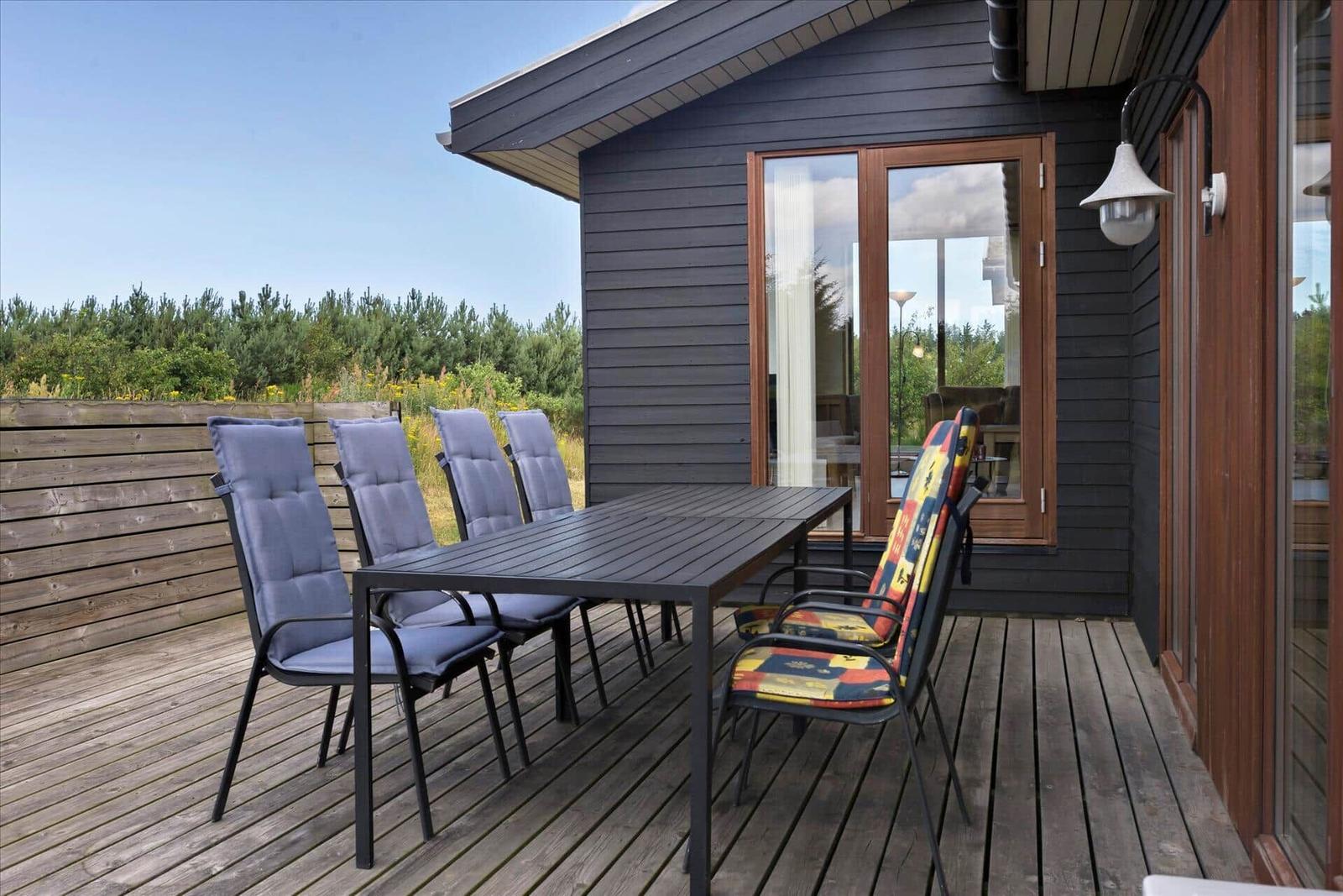 Terrasse mit Tisch und Stühlen vor einem Haus mit Holzverkleidung und Glasfront.