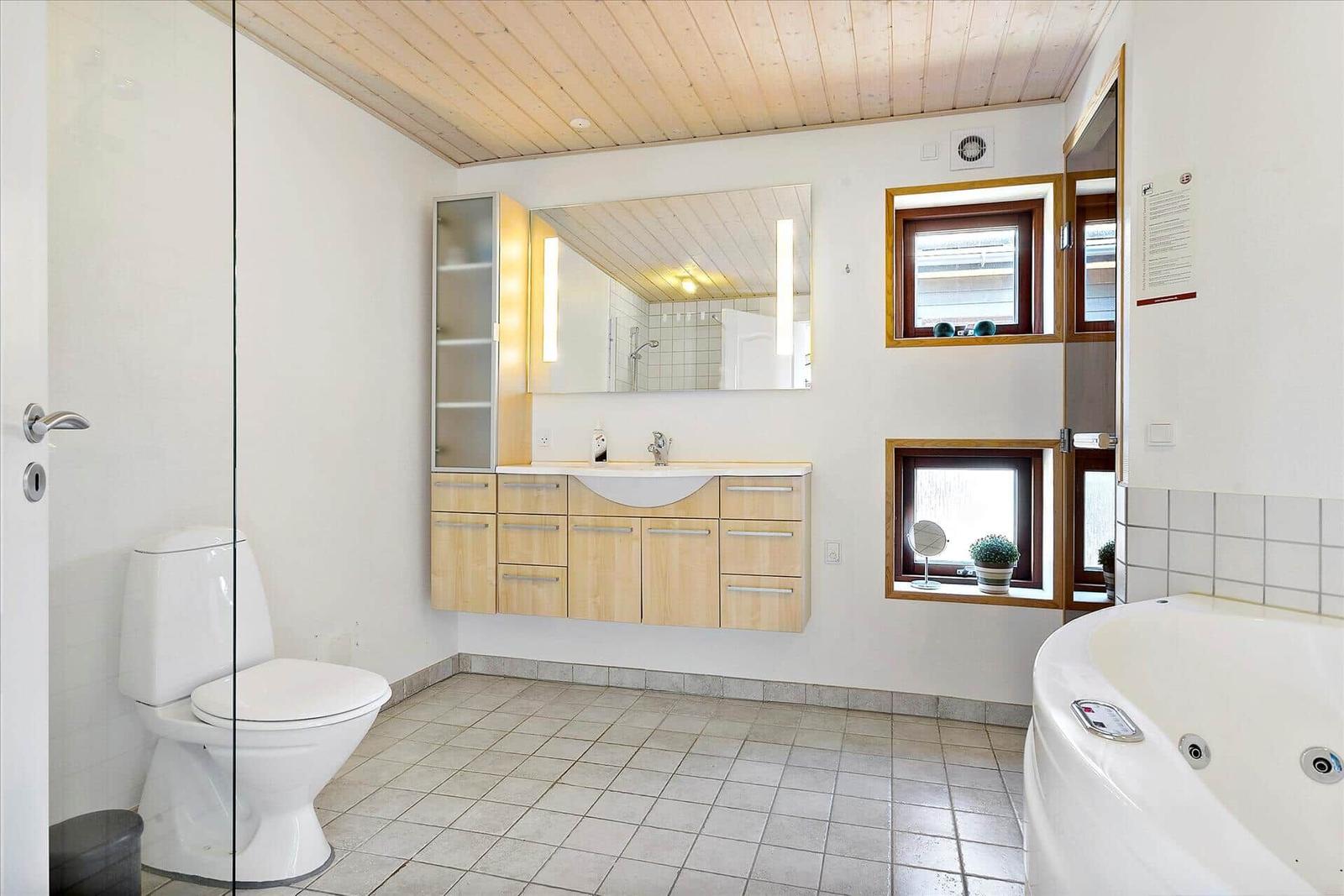 Bad mit Toilette, Waschbecken und Whirlpoolbad. Holzdecke und Fenster mit Pflanzen.
