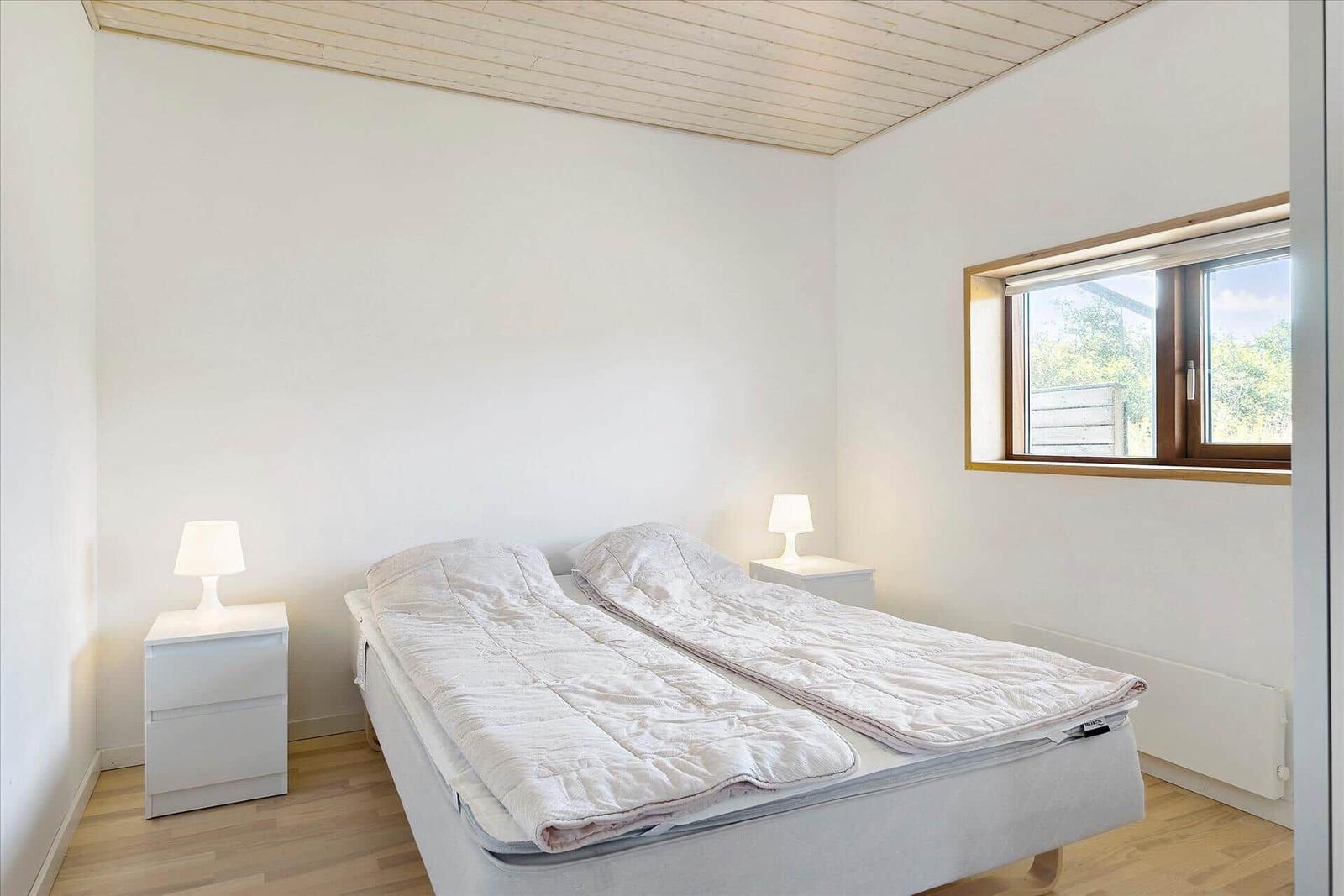 Schlafzimmer mit Doppelbett, zwei Nachttischen und Fenster mit Blick auf Außengelände.