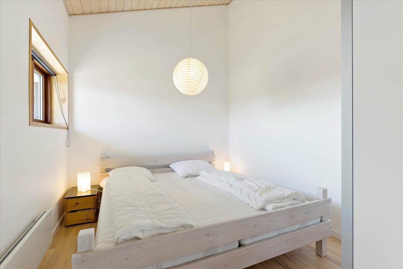 Schlafzimmer mit Holzbett, Nachttisch und Pendelleuchte.