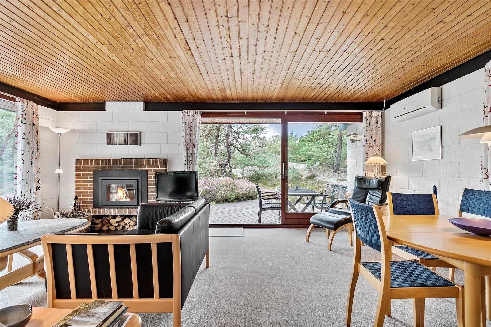 Wohn- und Essbereich mit Kamin, Holzdecke und Blick auf die Terrasse.