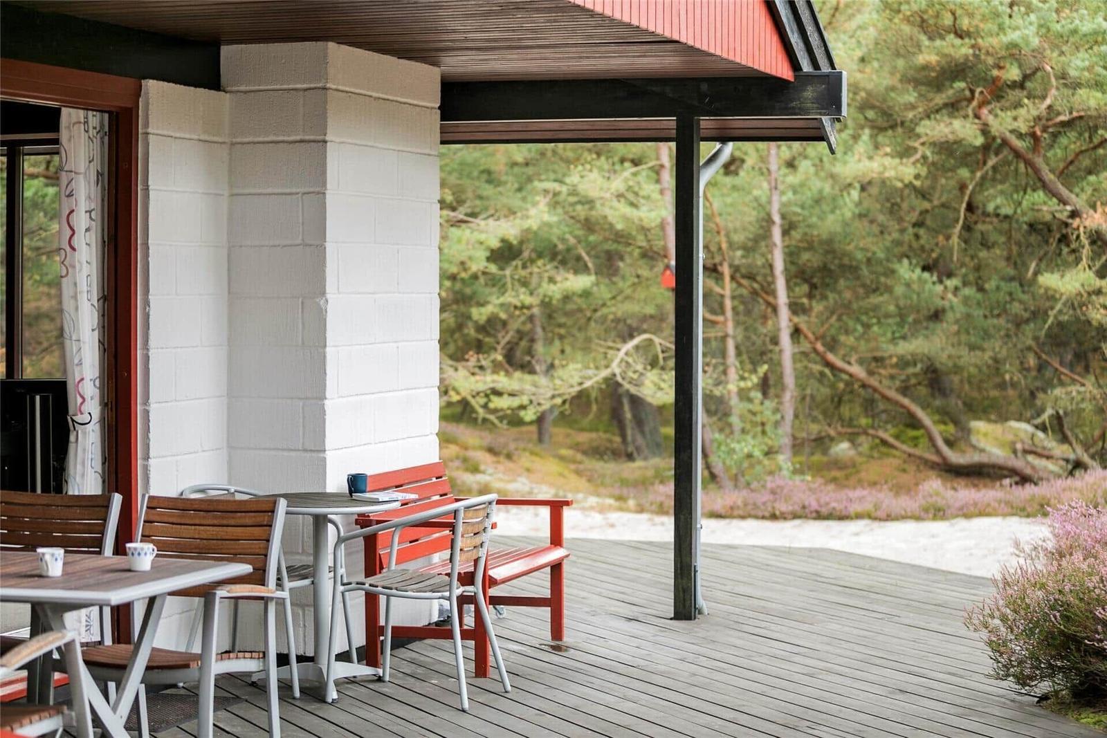 Terrasse mit Tischen, Stühlen und roter Bank. Hintergrund: Wald mit Heide.
