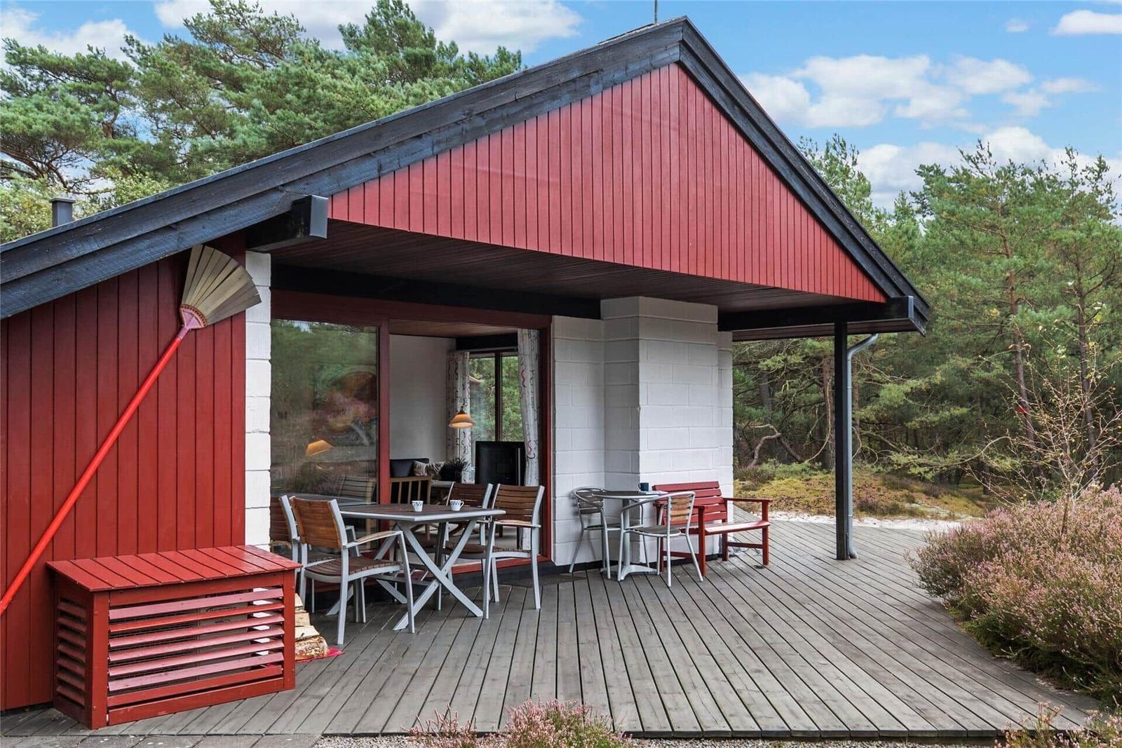 Rotes Holzhaus mit Terrasse, Tisch, Stühlen und Blick in den Wald.