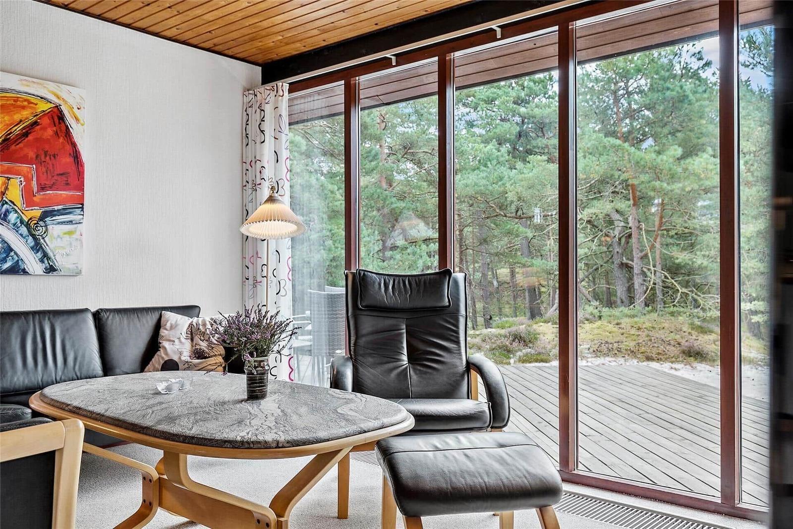 Wohnzimmer mit schwarzen Ledermöbeln, runden Tisch und Blick auf Wald.