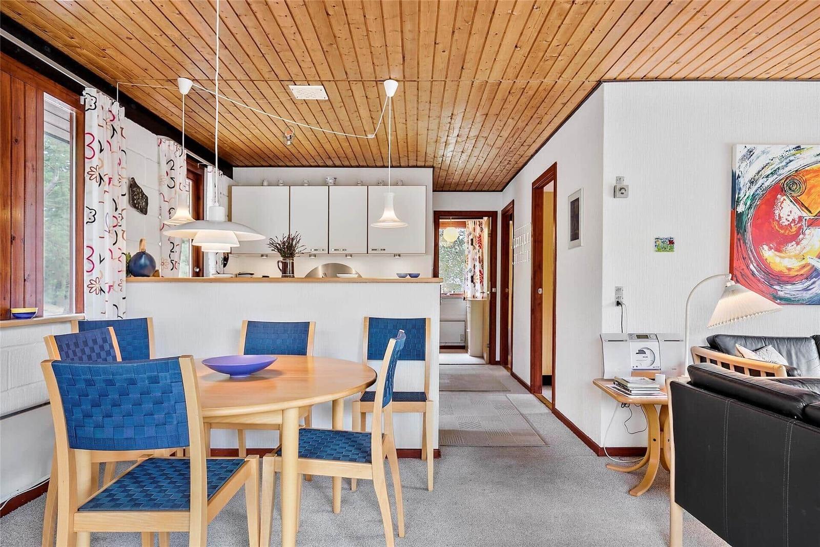 Ein Essbereich mit blauen Stühlen und einem runden Tisch. Küche und Wohnzimmer sind sichtbar.