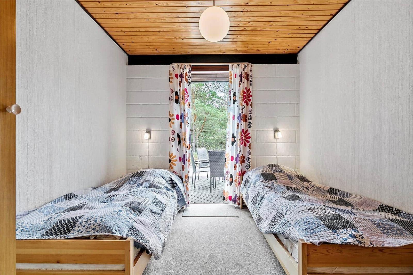 Zwei Betten mit gemusterten Bettdecken, Holzdecke und Blick auf Balkon mit Sitzgelegenheiten.