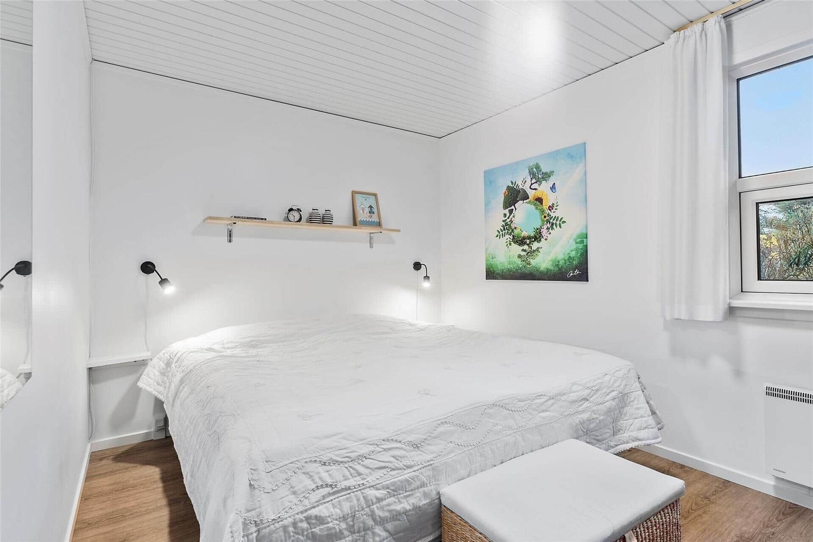 Schlafzimmer mit weißem Bett, Wandbild und Holzregal an der Wand.