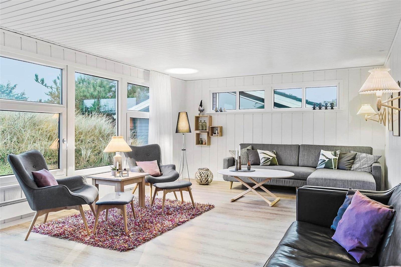 Wohnzimmer mit grauem Sofa, zwei Sesseln und großem Fensterblick.