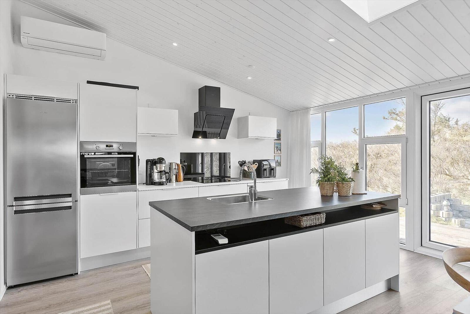 Moderne Küche mit Kücheninsel, Edelstahlkühlschrank und Blick auf Außenbereich.