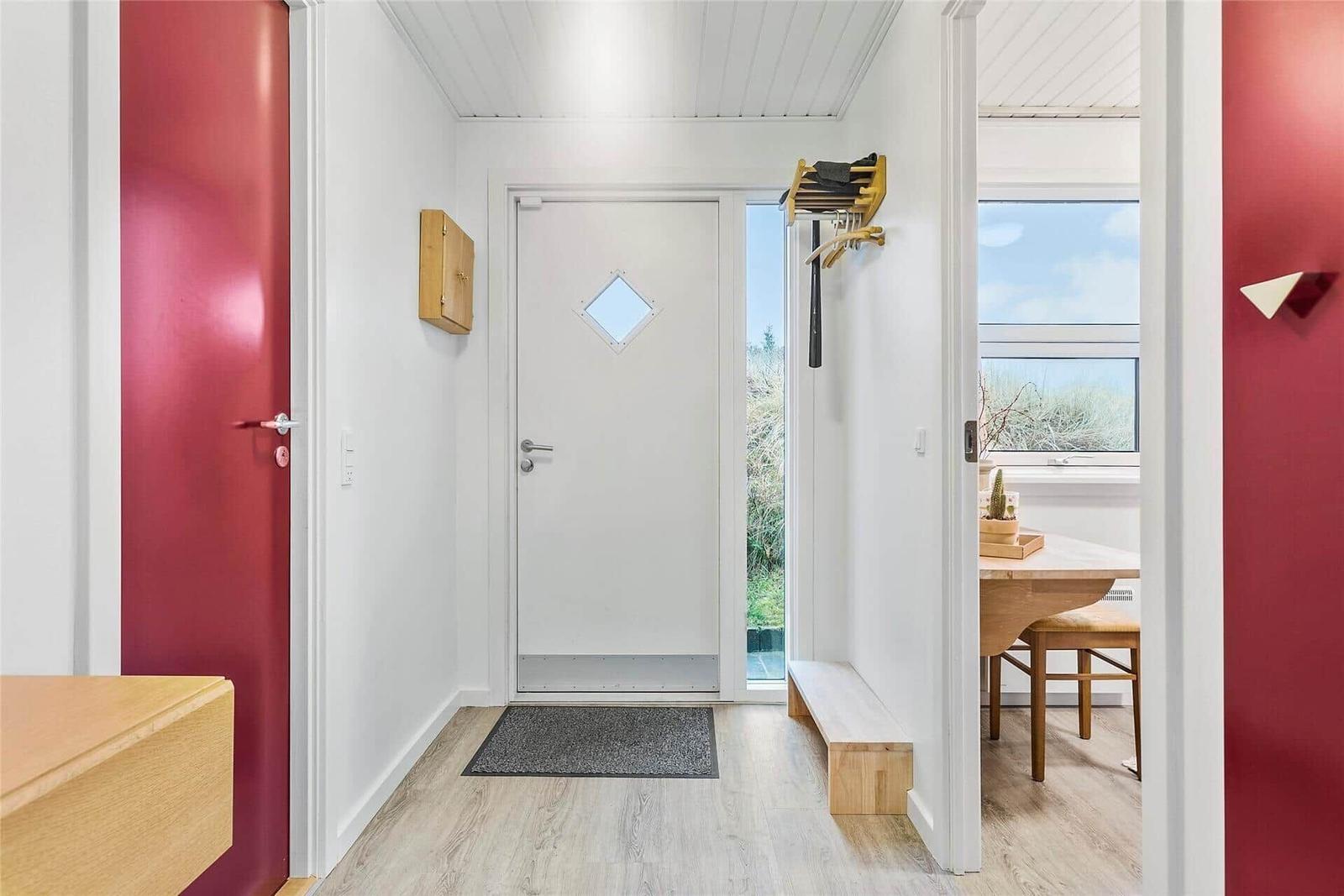 Eingangsbereich mit roter Tür und Blick in Esszimmer mit Tisch und Stühlen.