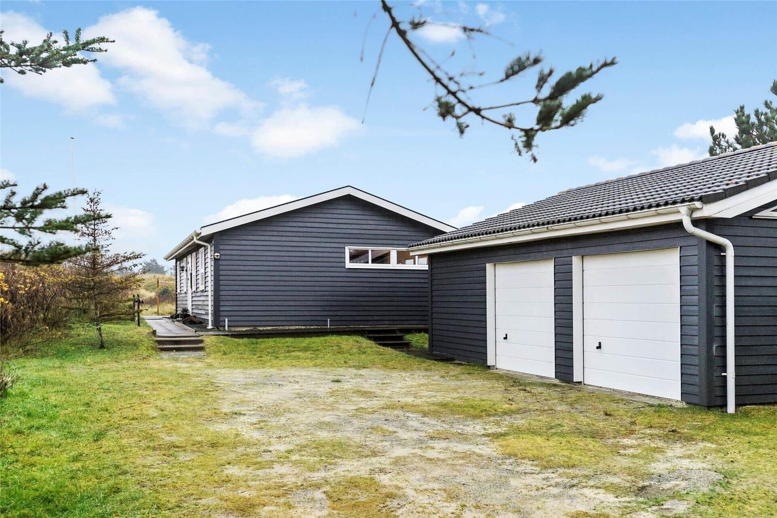 Ein graues Haus mit Garage und Garten unter blauem Himmel.