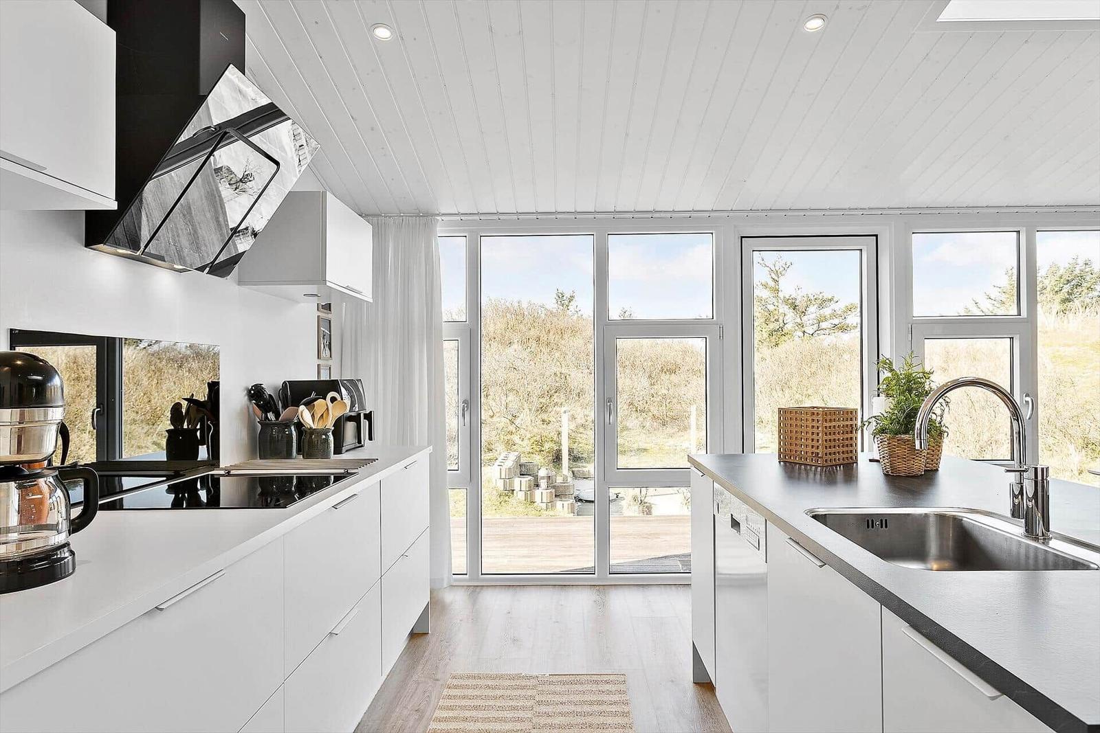 Moderne Küche mit weißen Schränken und großem Fensterblick auf den Außenbereich.