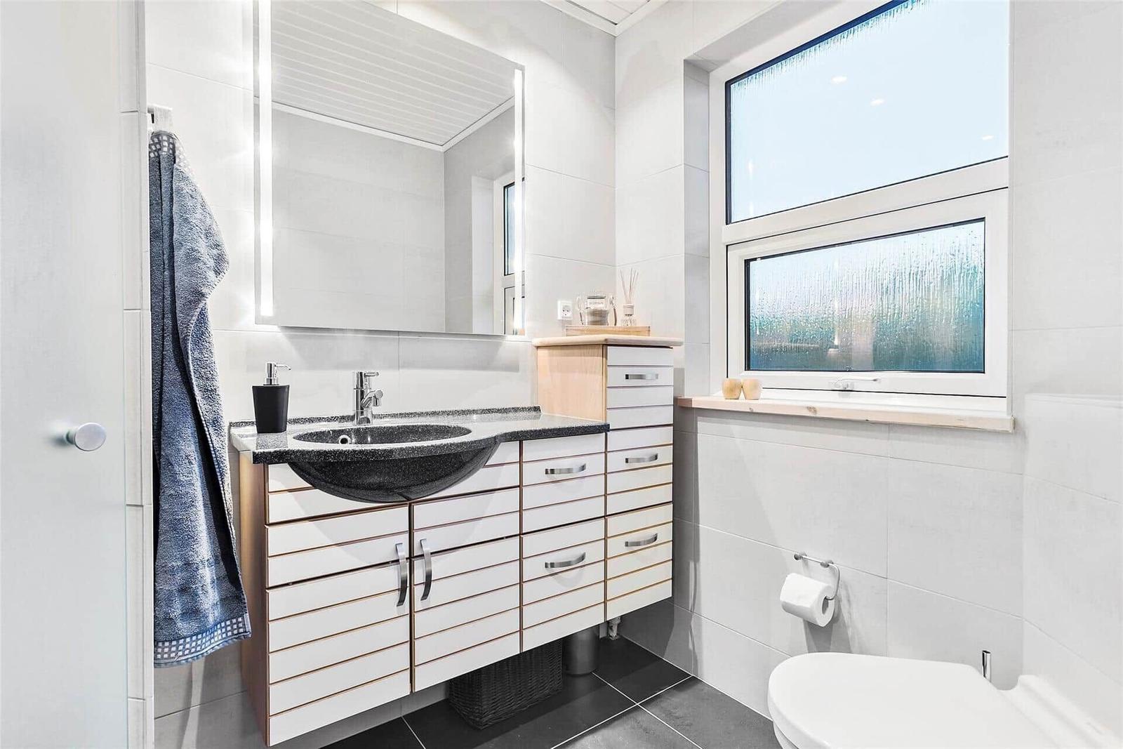 Badezimmer mit Waschbecken, Spiegel, Toilette und Fenster.