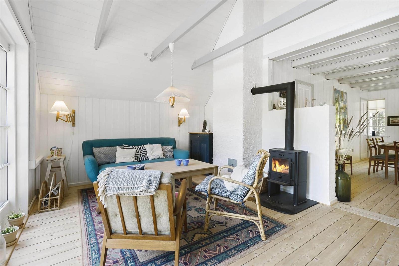 Wohnzimmer mit Kamin, Sofa und Holzboden. Blick in die Küche.