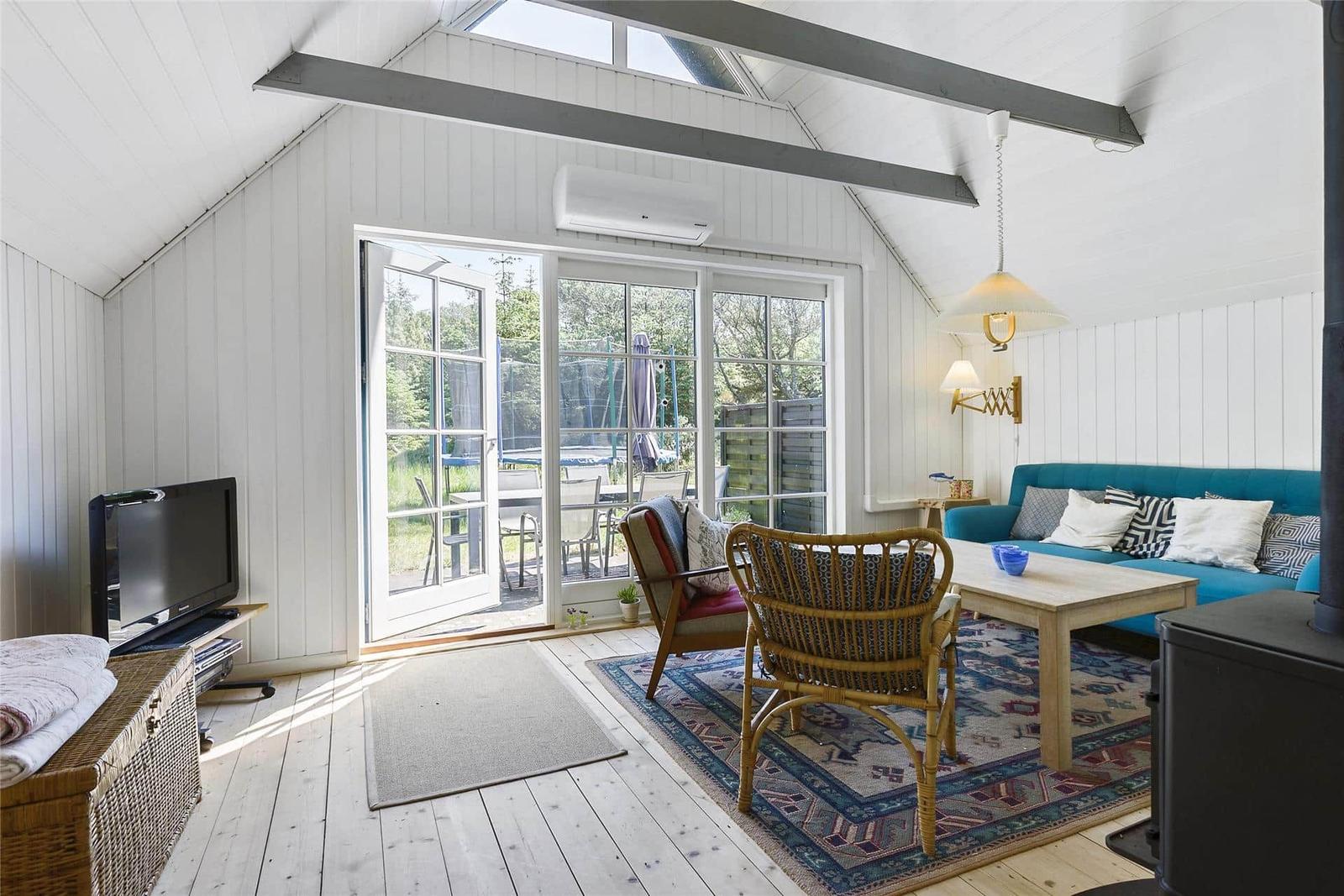 Wohnraum mit Sofa, Stühlen und Blick auf Garten. Holzboden und weiße Wände.