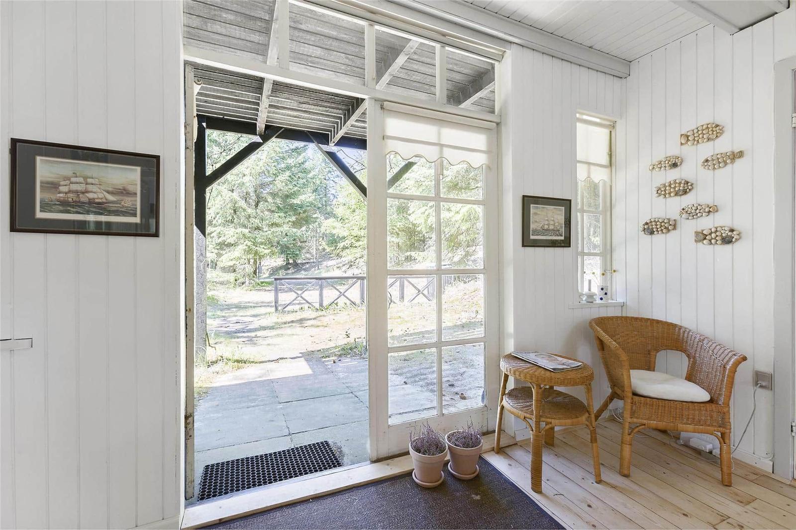 Eingangsbereich mit Rattan-Sessel, Pflanzen und Blick auf den Garten.