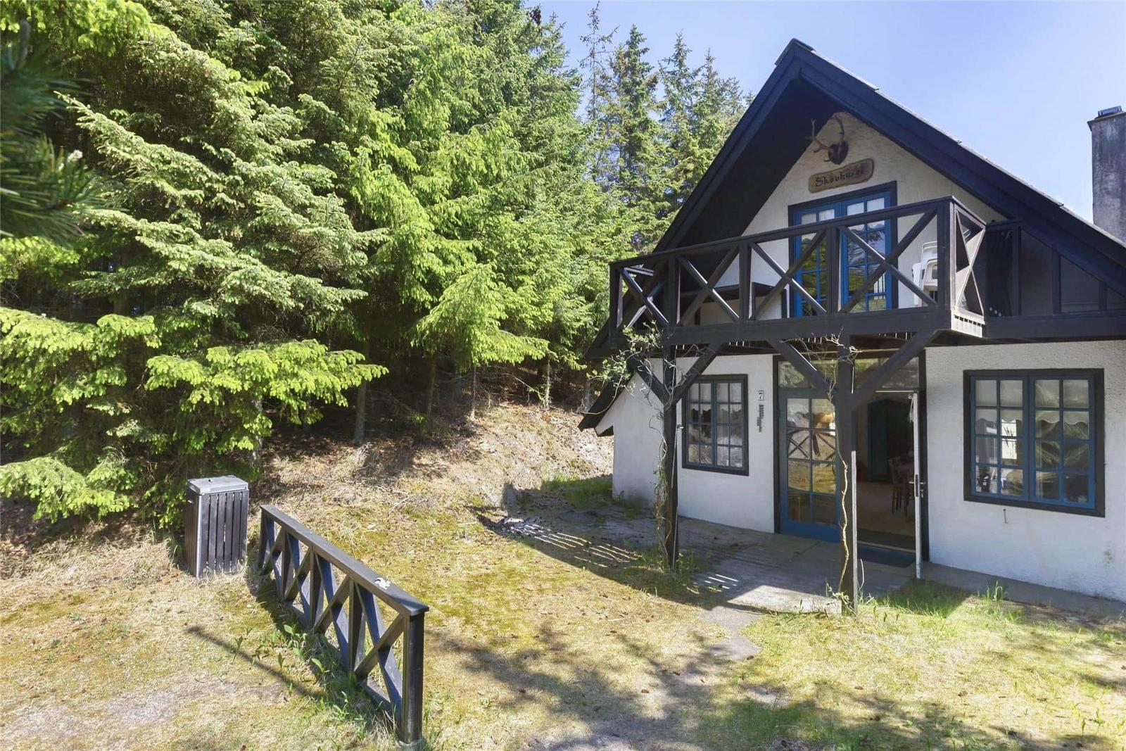 Haus mit Balkon, blauen Fenstern und Wald im Hintergrund.